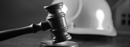 Foto eines Richterhammers auf einem Holztisch mit einem weißen Helm im Hintergrund